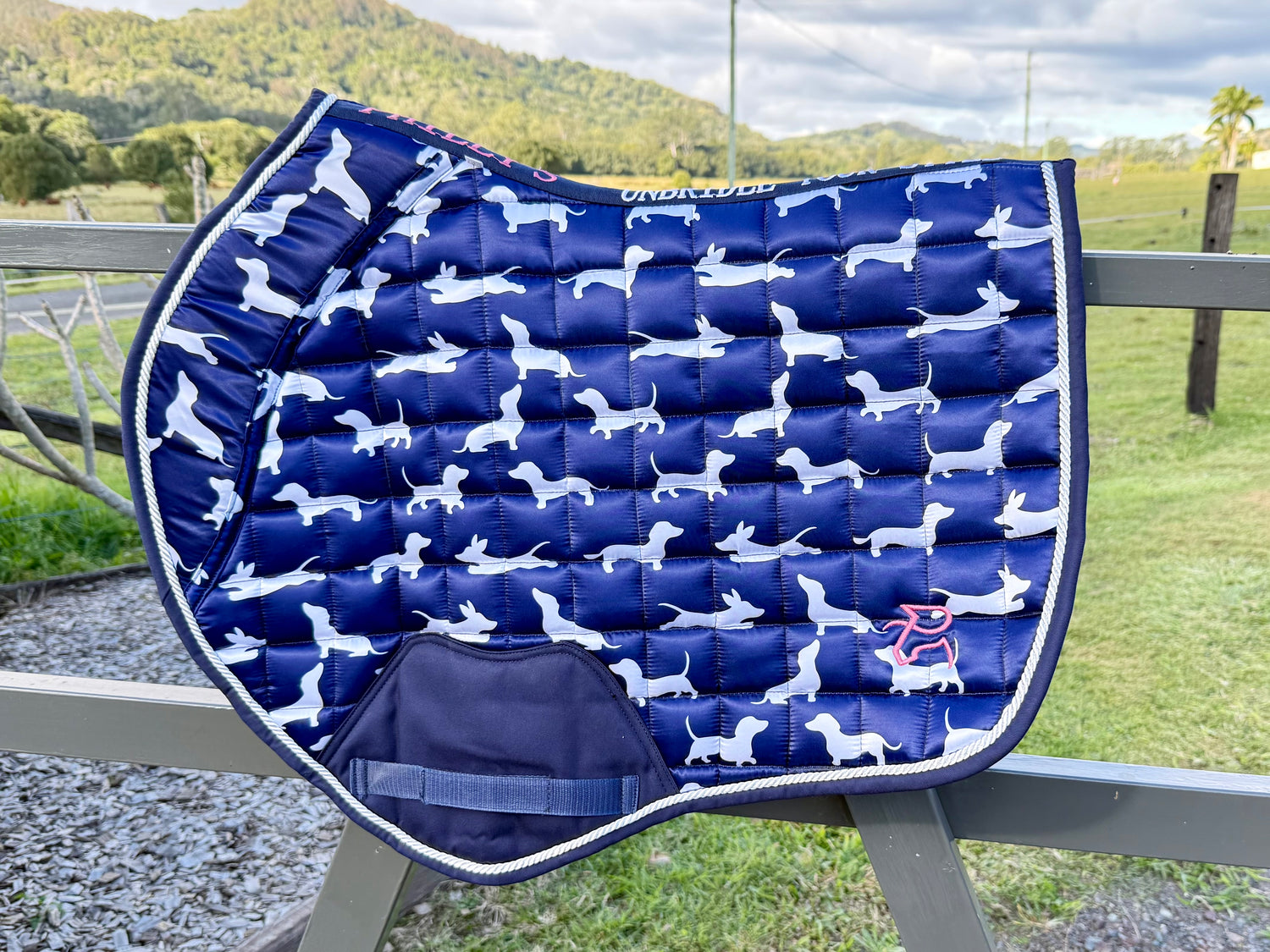 The Snag jump saddle pad draped on a rail with paddock behind